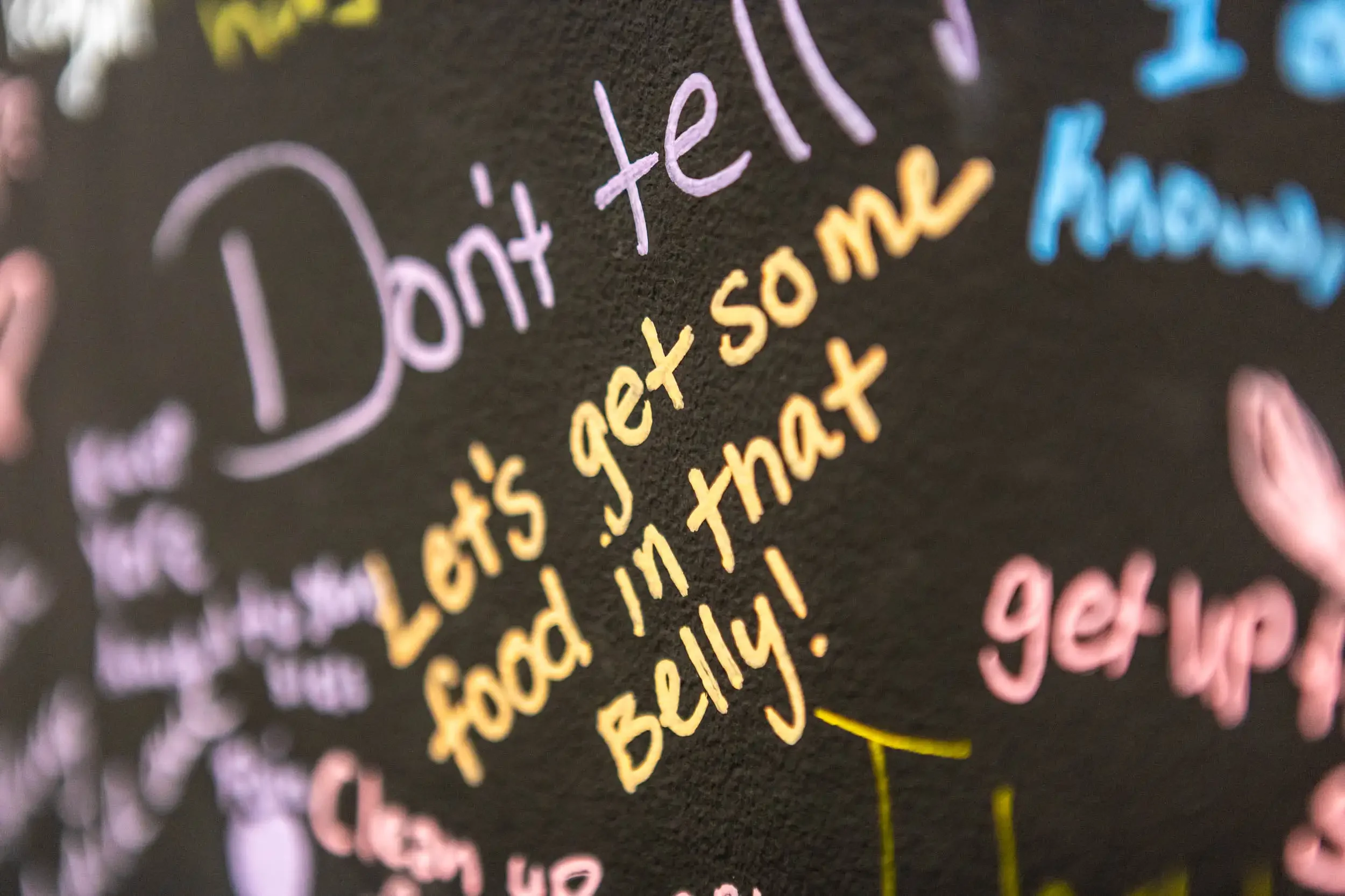 Close-up of colorful handwritten text on a black background, with the phrase "hot tell" visible in pink and yellow