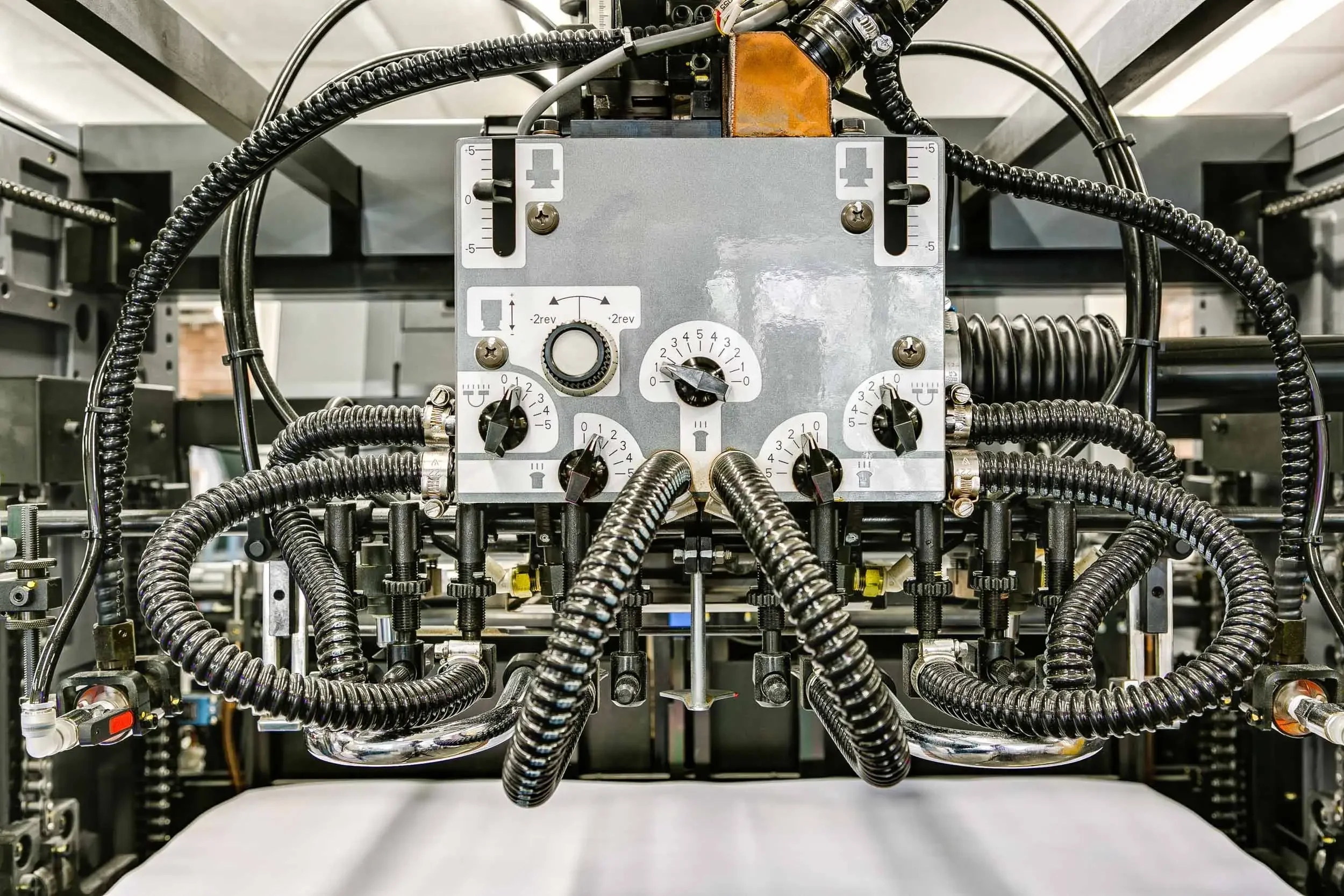 Close-up of a complex industrial control panel with various control knobs, dials, and thick black flexible conduits, likely part of a machinery or manufacturing system.