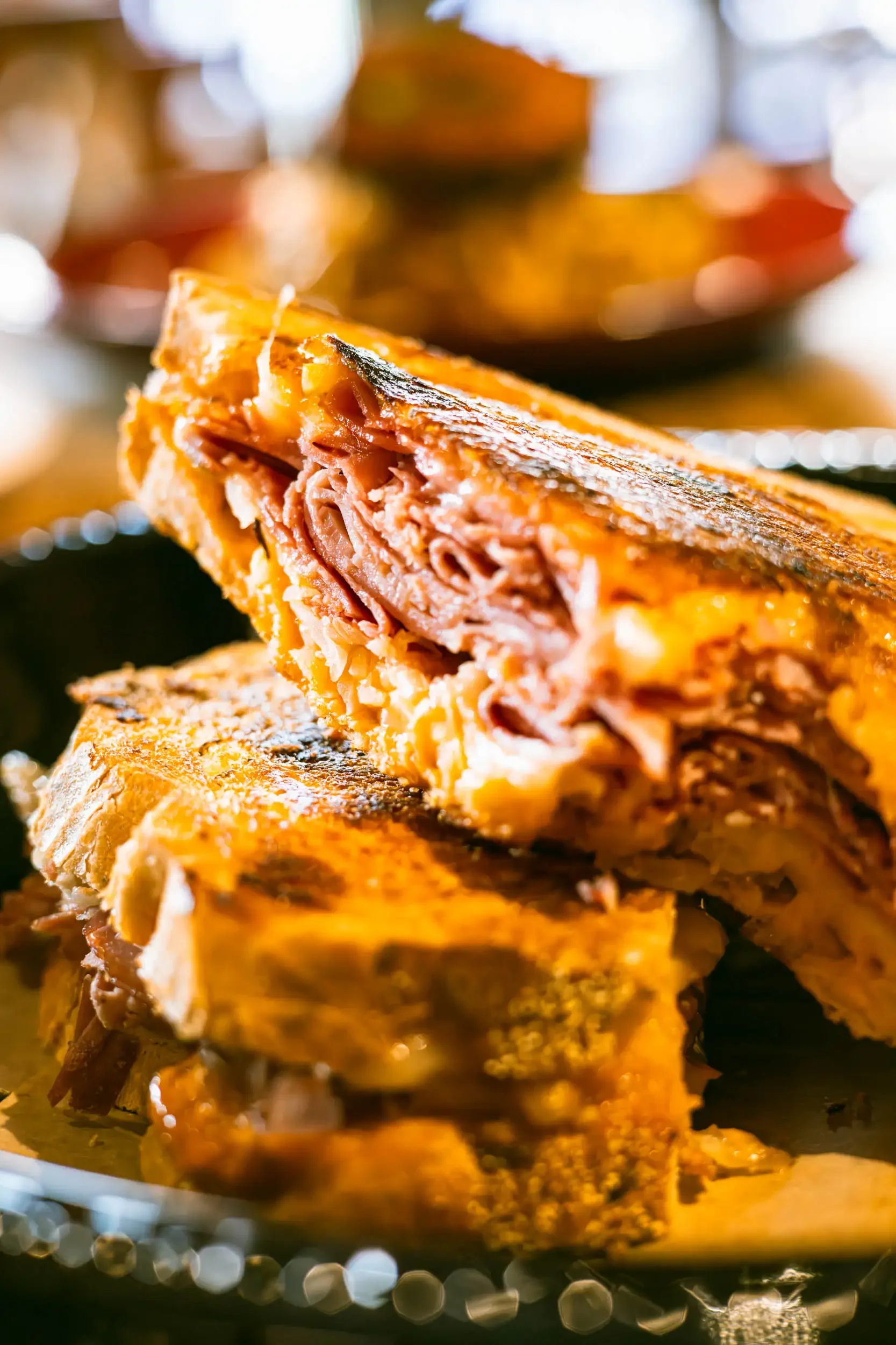 A close-up of a slice of meatloaf with a crispy crust, showing a moist, meaty interior. The background features blurred warm lights, creating a cozy atmosphere.