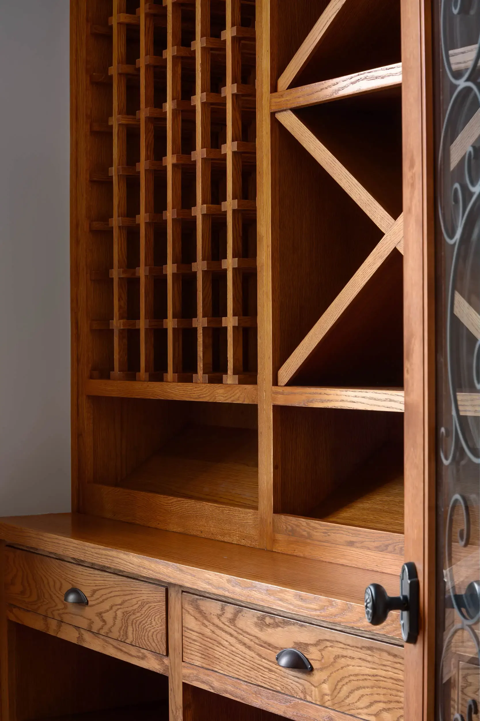 A large wooden wine rack with multiple compartments and small drawers at the bottom, situated on a wooden surface.