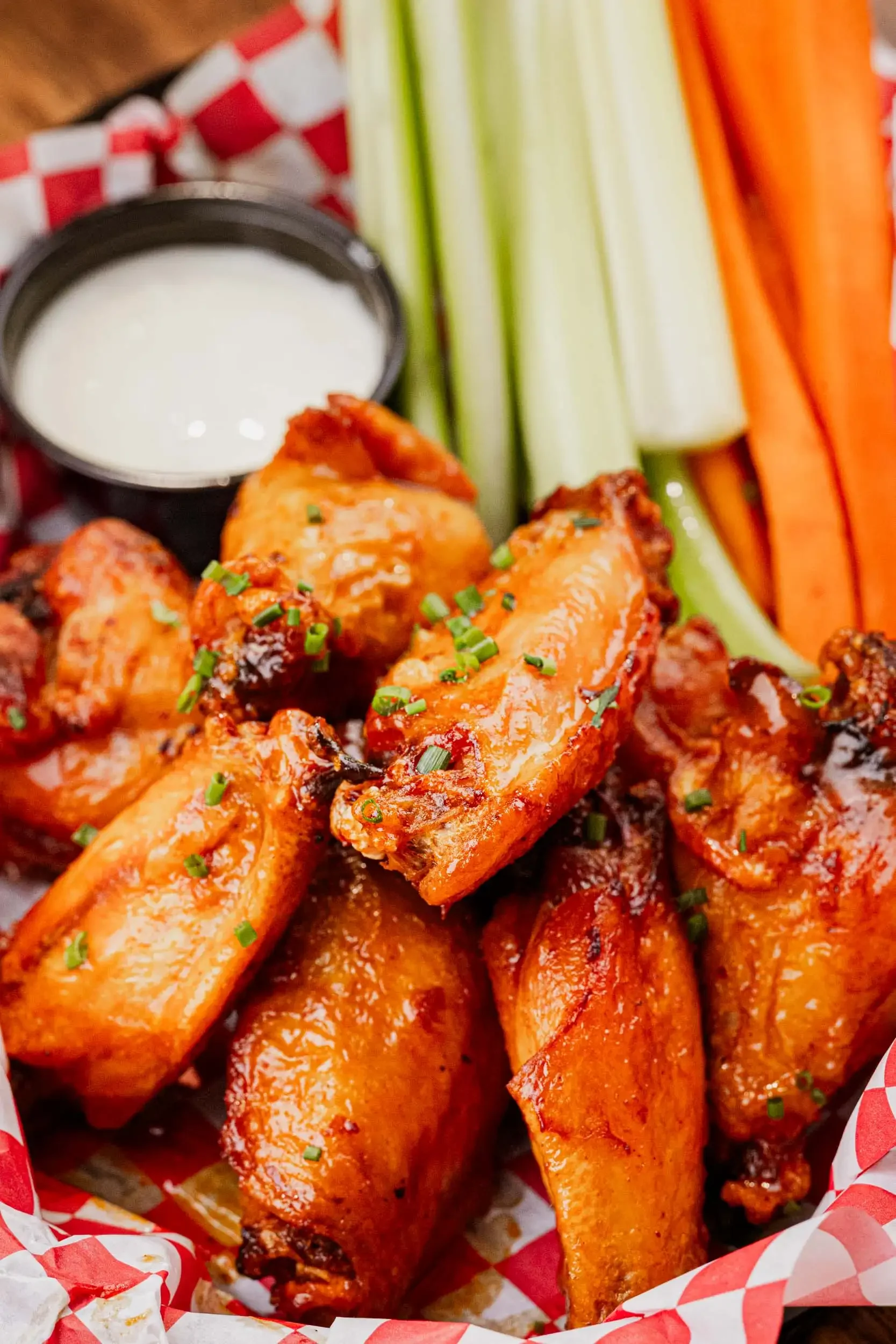 Close-up of spicy buffalo chicken wings garnished with chopped green onions, served with a side of ranch dressing, and fresh celery and carrot sticks on the side.