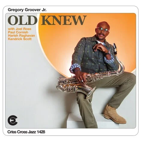 Man in a blazer and khakis sitting on a white cube, holding a saxophone, smiling against an orange and white background, album cover for Gregroy Groover Jr.'s 'Old Knew' with featured artists Joel Ross, Paul Cornish, Harish Raghavan, and Kendrick Sco