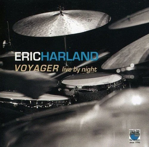 Album cover for Eric Harland's "Voyager Live by Night," featuring blurred drum set with cymbal and drumsticks, and a dark background with text.