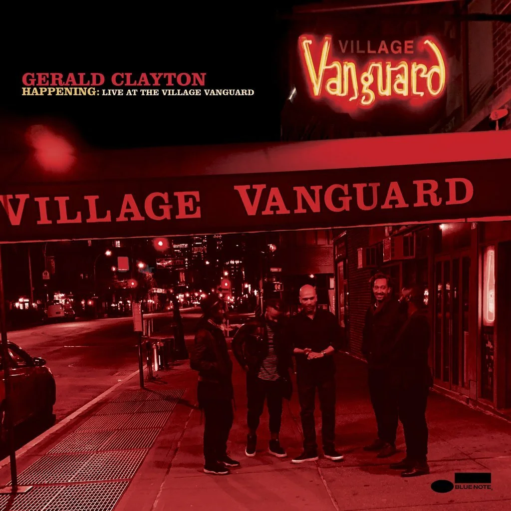 Four men standing under a red illuminated sign that says 'Village Vanguard' on a city street at night. The scene has a red tinted filter.