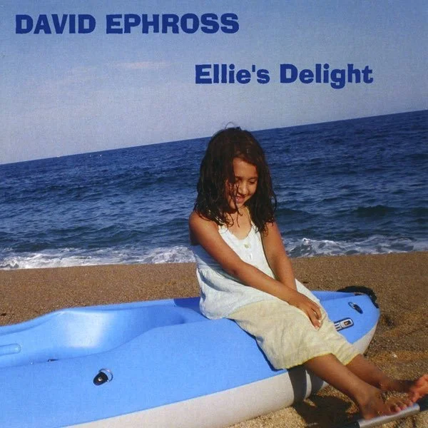 A young girl sitting on a blue and white kayak on a sandy beach, with the ocean and a clear sky in the background. The text on the image reads 'David Ephross' and 'Ellie's Delight'.