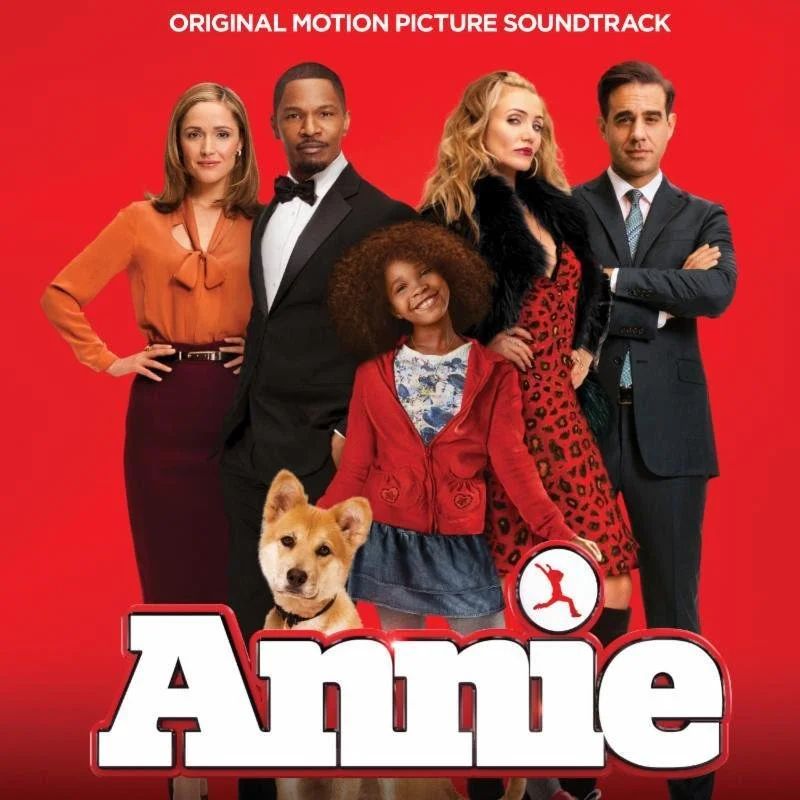 Poster for the movie "Annie" featuring four adult characters, a young girl, and a dog against a red background. The title "Annie" is at the bottom with a circular logo of a dog jumping through a hoop.