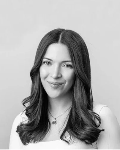 Black and white portrait of a woman with long, wavy hair, smiling softly, wearing a necklace and a sleeveless top.