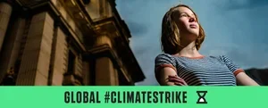 A young girl standing outdoors with a building behind her and a partly cloudy sky, holding a sign with the text 'Global #ClimateStrike.'