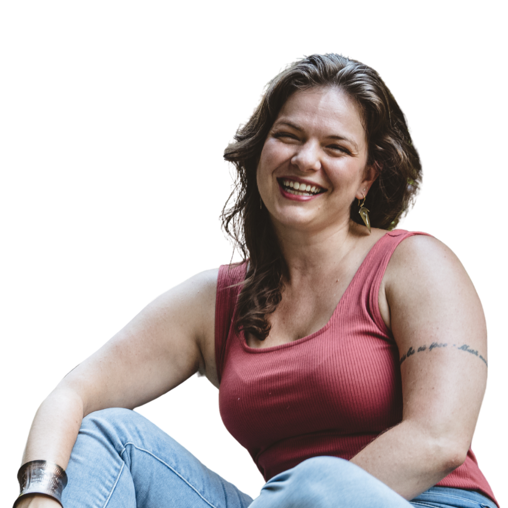 A woman smiling, wearing a sleeveless red top and light blue jeans, sitting with her arm resting on her knee.