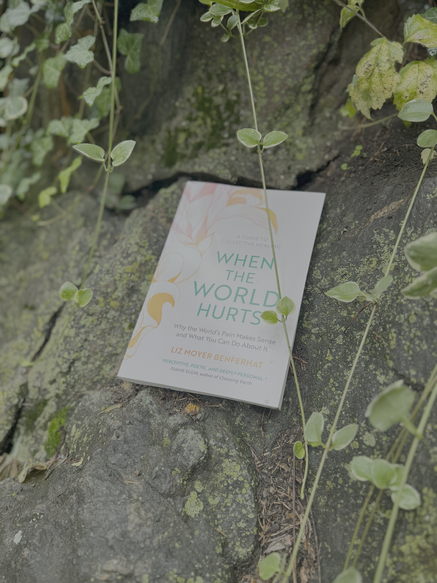 A book titled 'When the World Hurts' resting on a mossy rock with green vines and leaves surrounding it.