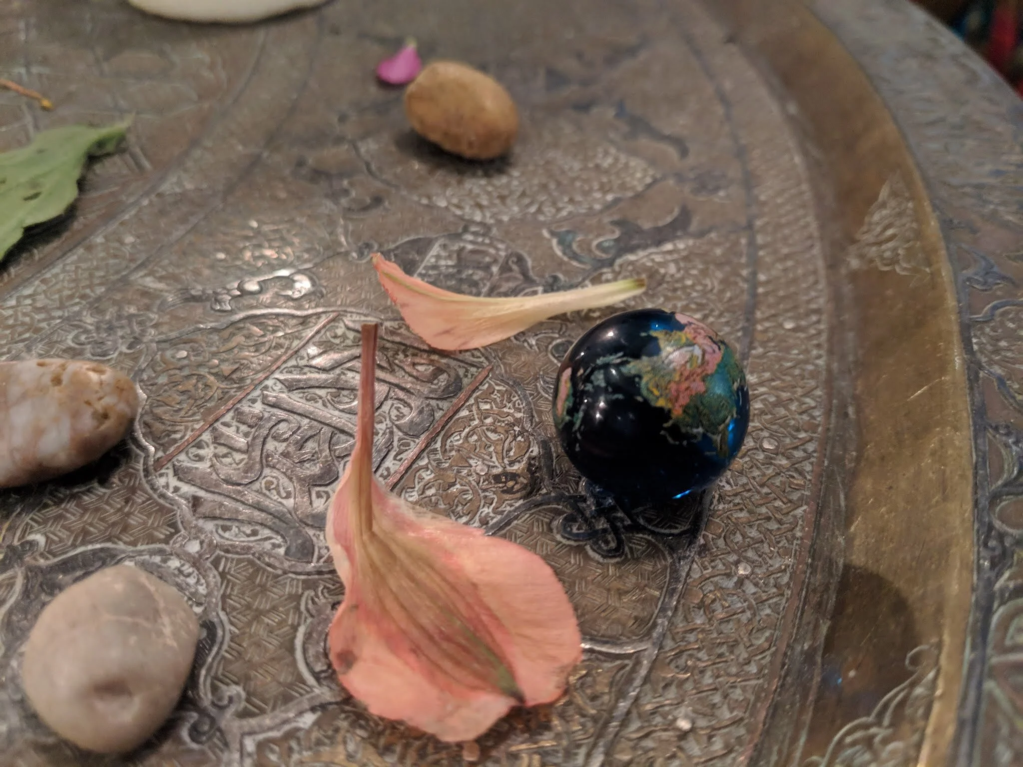 Decorative surface with small rocks, dried flower petals, and a glossy black globe with colorful landmasses.