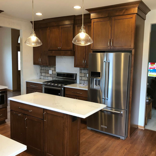 Kitchen with wooden cabinets, a marble island, a stainless steel refrigerator, and a stove. Two pendant lights hang over the island.