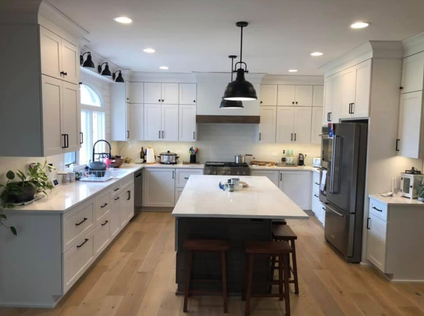 Modern kitchen with white cabinets, a large central island, stainless steel appliances, and black pendant lighting.