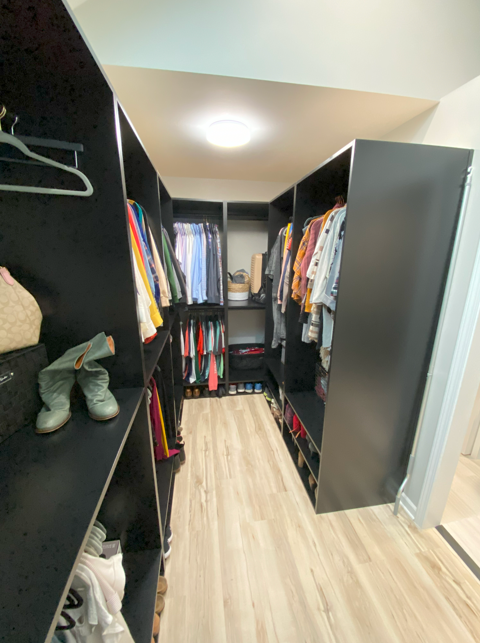 Walk-in closet with black shelves filled with clothes, shoes, and accessories, and a light-colored wooden floor.