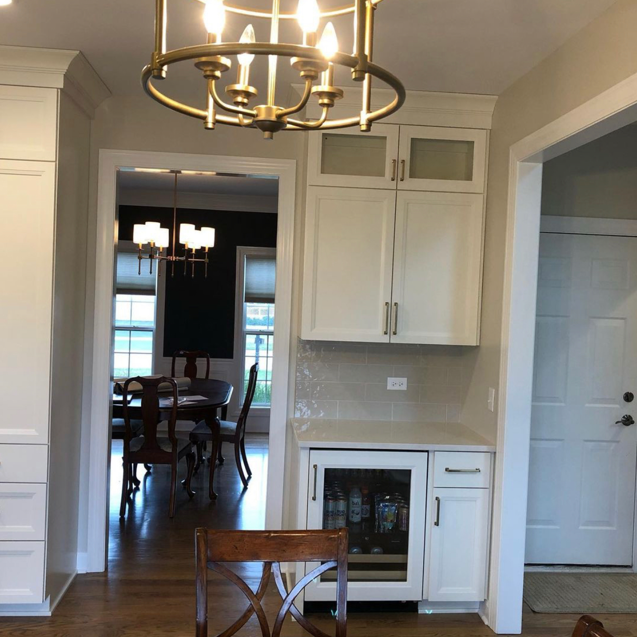 Kitchen with white cabinets, a built-in wine cooler, and a chandelier hanging from the ceiling, connecting to the dining area with a wooden table and chairs.