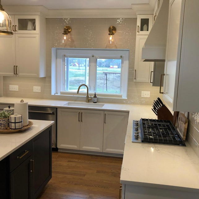 Bright kitchen with white cabinets and a window above the sink, modern light fixtures, and a gas stove with a knife block nearby.