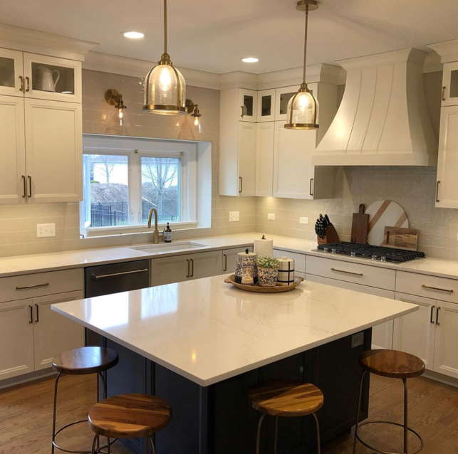 Modern kitchen with white cabinets, a large central island with a white countertop, wooden stools, a window above the sink, and pendant lighting.
