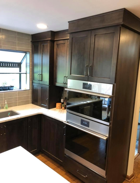 Kitchen with dark wooden cabinets, a window with a black frame, a white countertop, and built-in stainless steel oven and microwave.