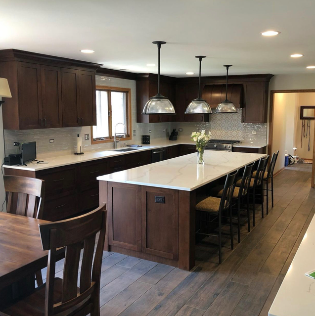 Modern kitchen with dark wood cabinets, a large white island with seating, three pendant lights, and a window above the sink.
