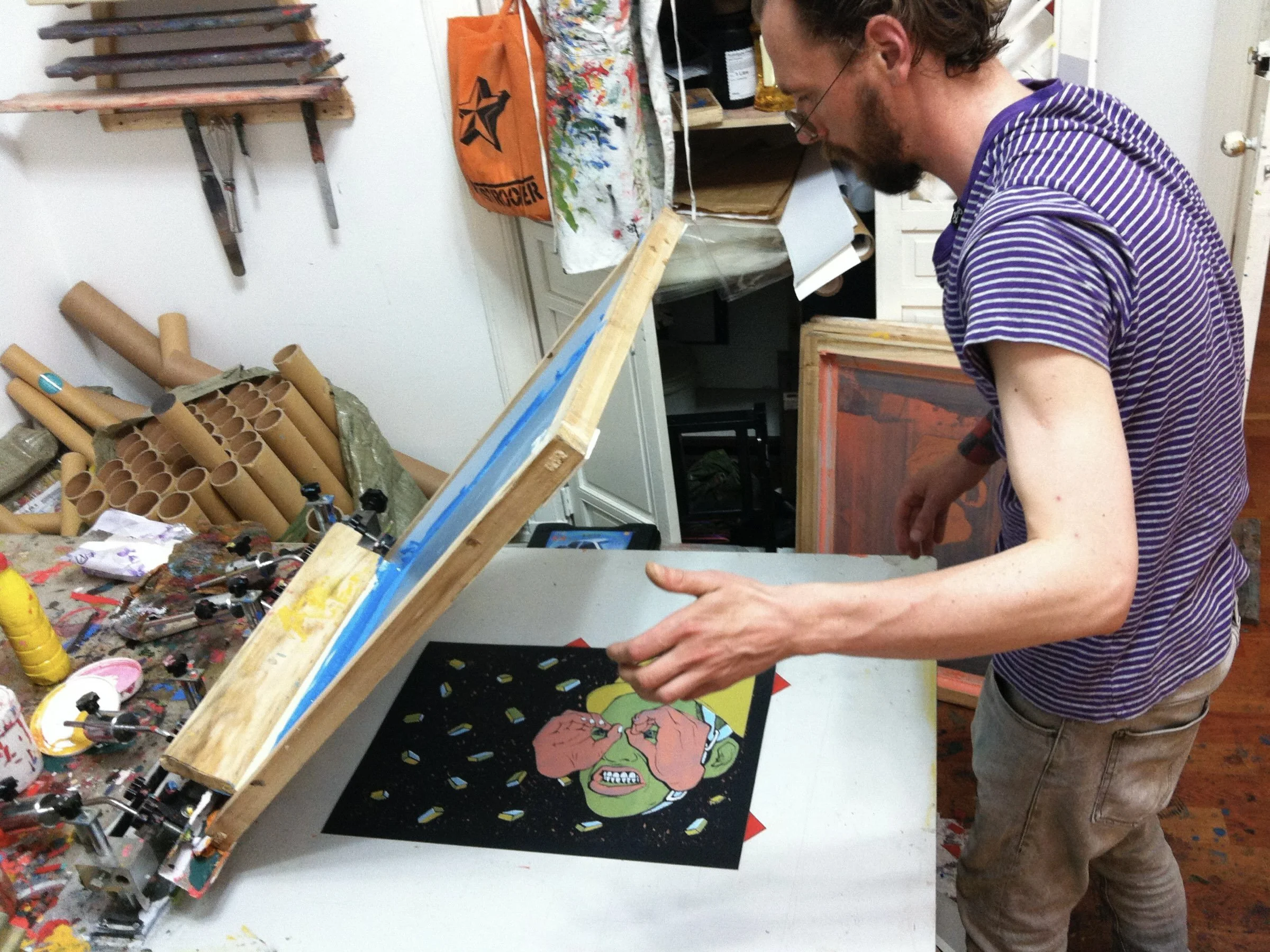 Artist hand-pulling a screen print of the "Eyes Wide Open" design in the studio.