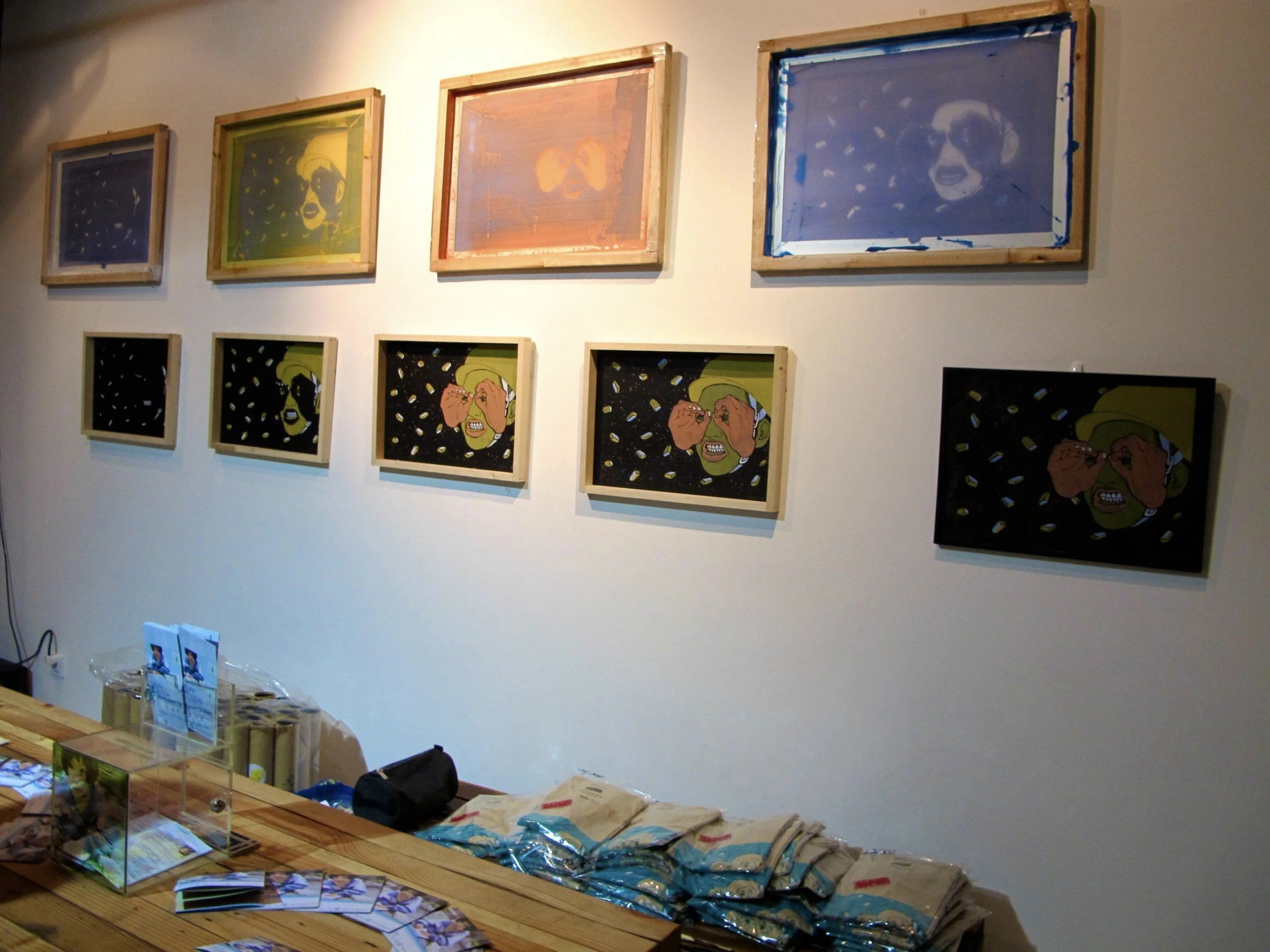 Gallery display featuring framed "Eyes Wide Open" prints and folded tees on a table.