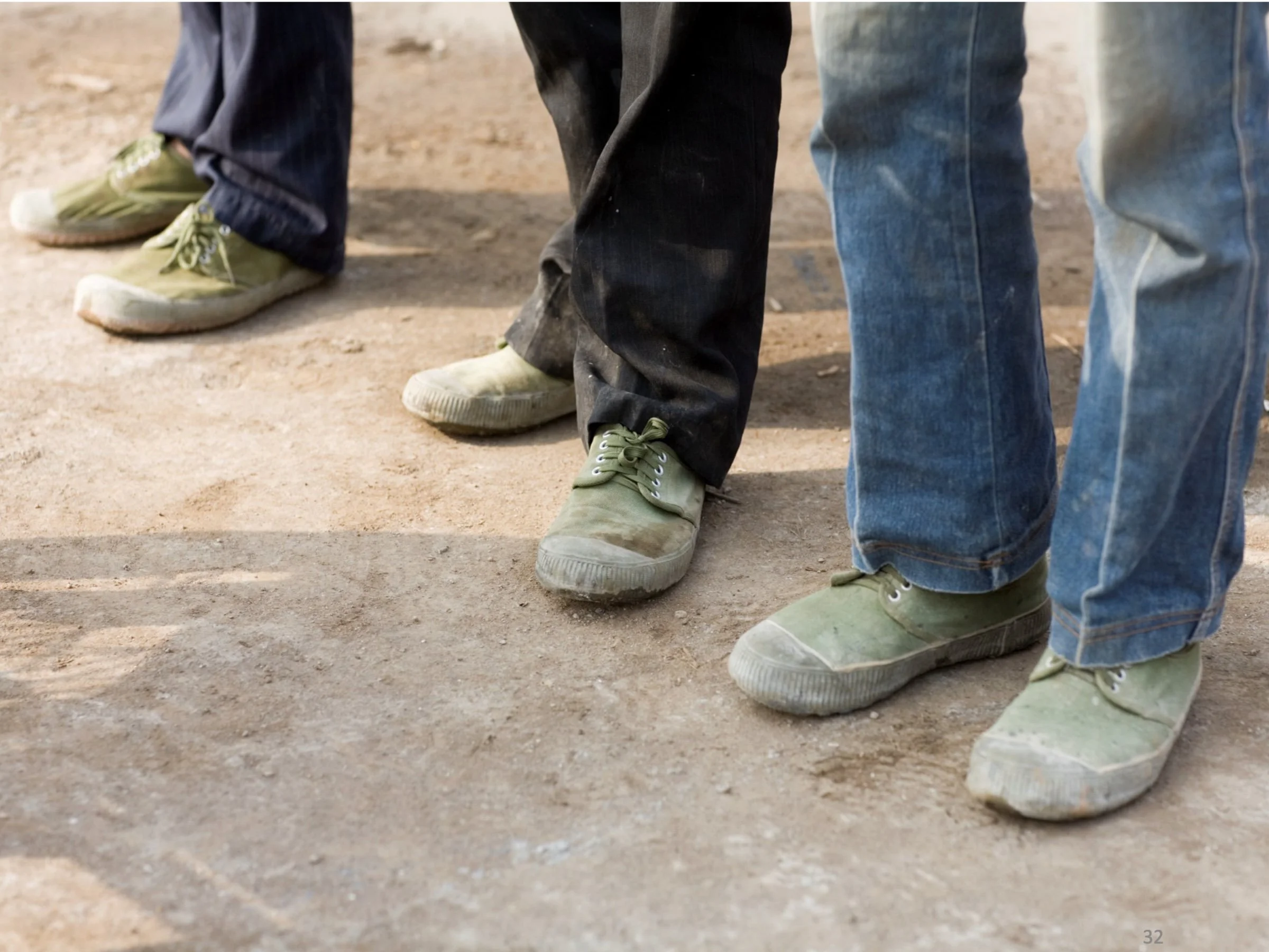 Close up of three Chinese construction workers wearing worn green Ospop rubber soled shoes on a dusty ground.