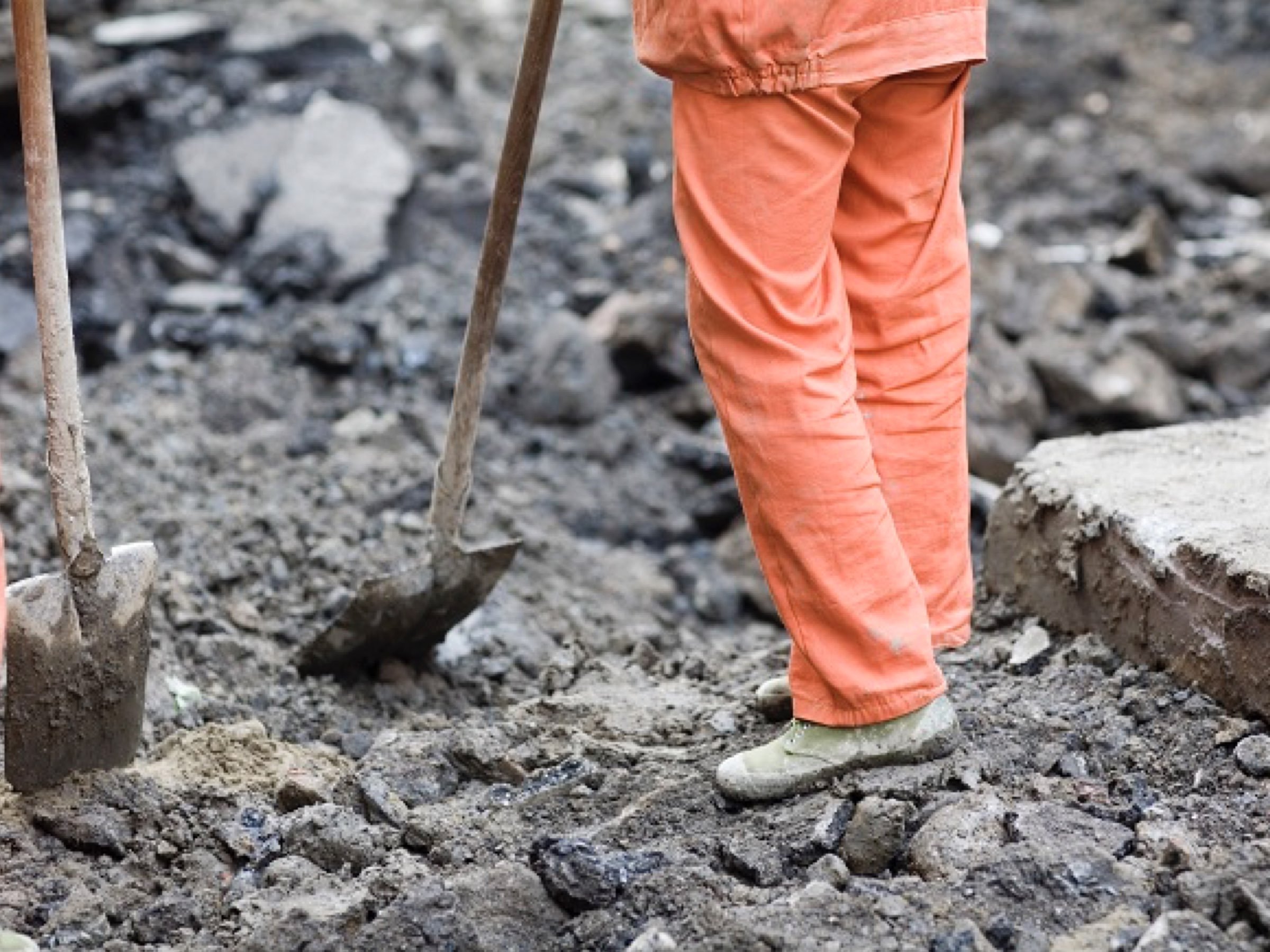 Worker in bright orange coveralls and green Ospop shoes standing on rubble at a demolition site.
