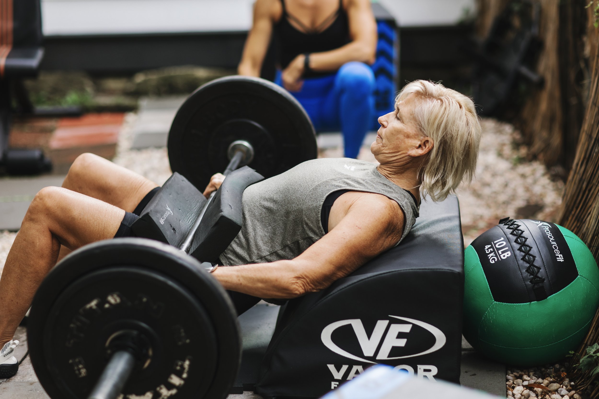 Trainer coaching a client through a barbell hip thrust, emphasizing proper setup, alignment, and controlled movement.
