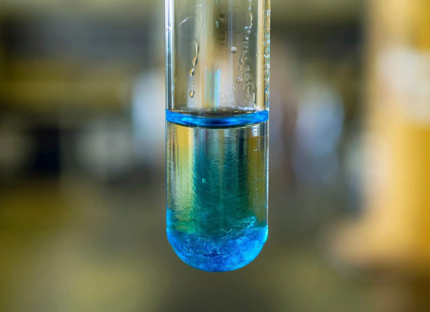A close-up photograph of a test tube filled with a blue liquid, with the background blurred