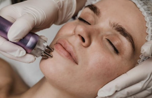 A woman receiving a facial treatment with a device on her face, lying with eyes closed.
