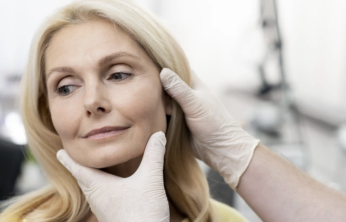 A woman receiving a facial examination from a healthcare professional wearing gloves in a clinical setting.