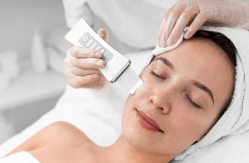 A woman receiving a facial treatment with a skincare device on her forehead.