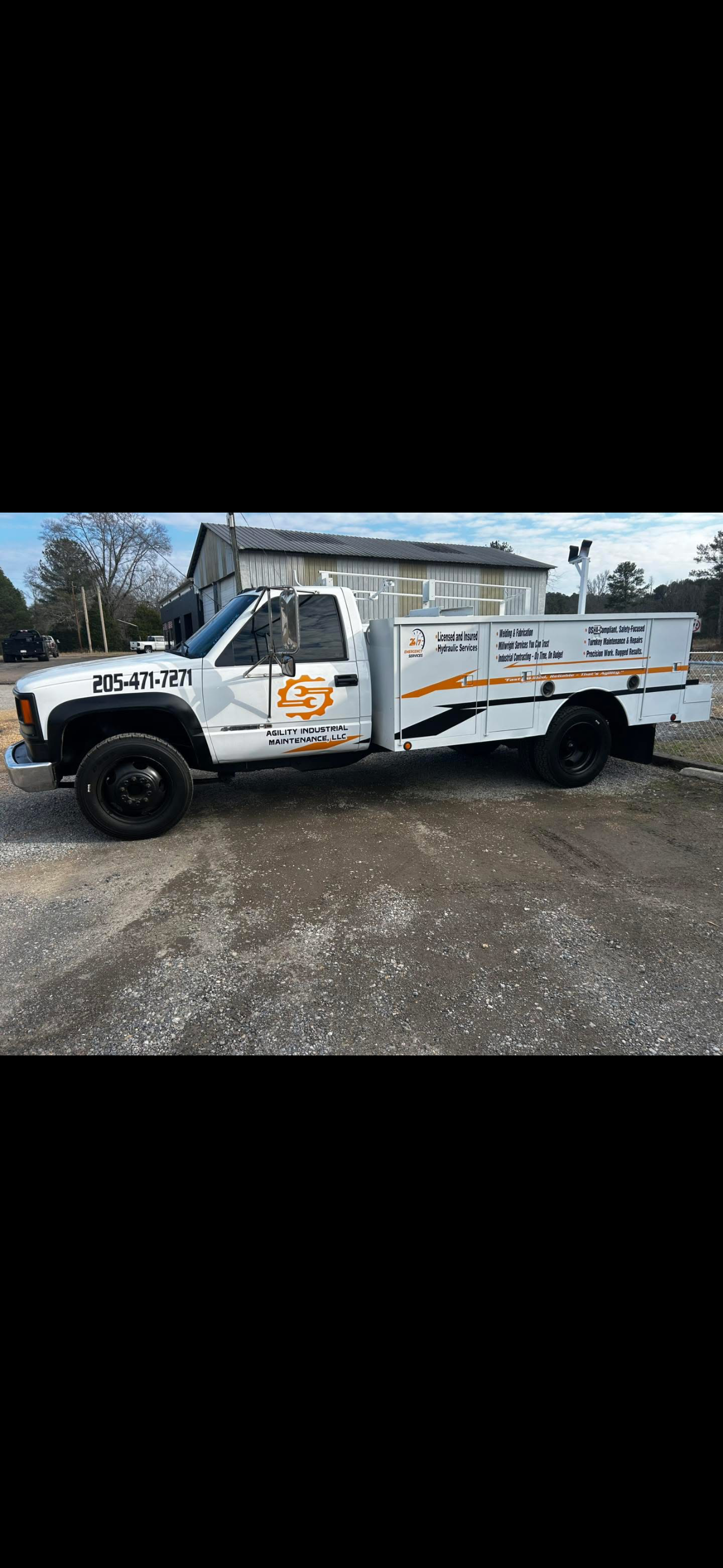 White industrial maintenance truck with company logo and contact information parked on gravel in front of a building with a metal roof.