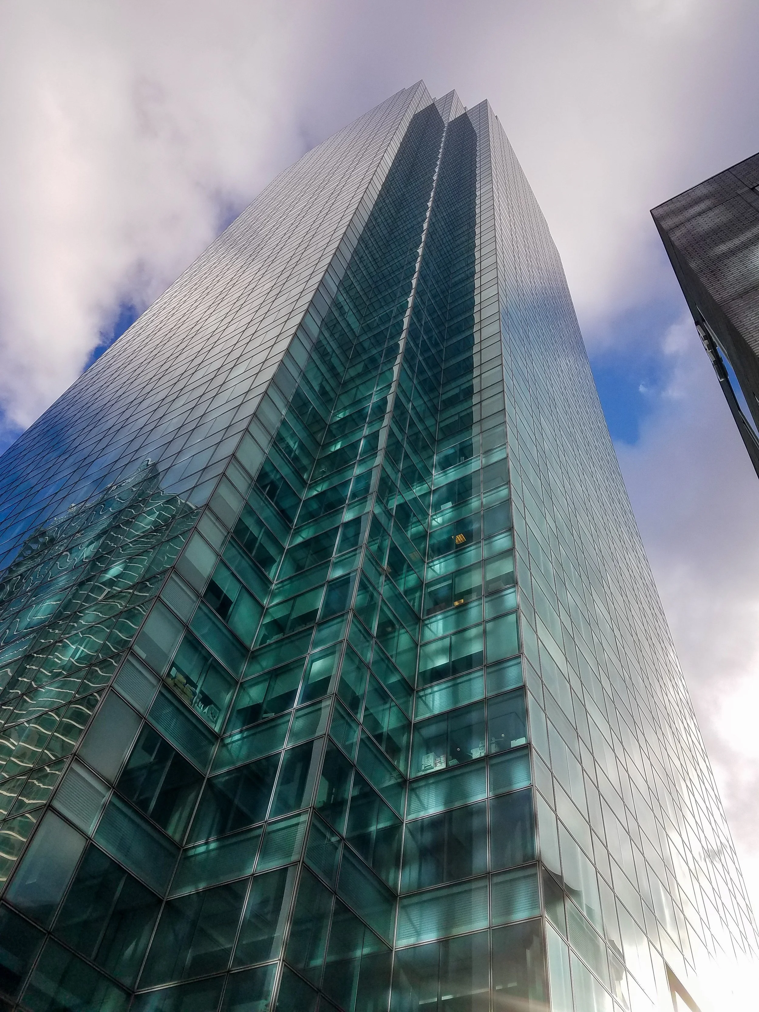 An image of a glass-fronted skyscraper poking towards the clouds.