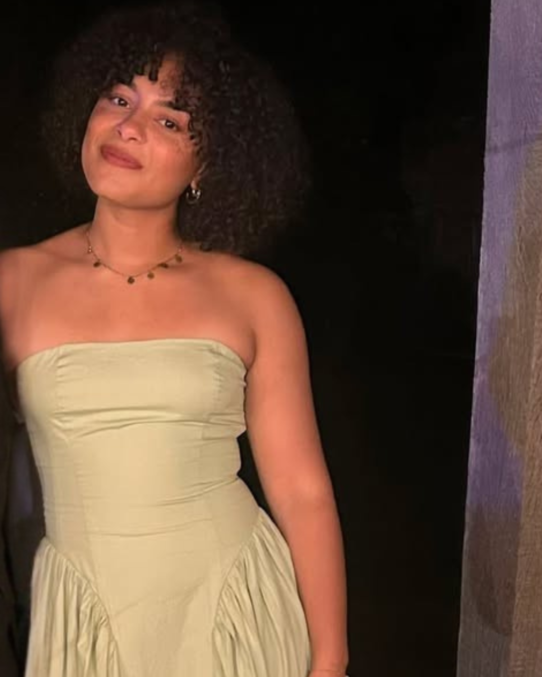 A black lady with curly black hair smiling in a green dress at night time