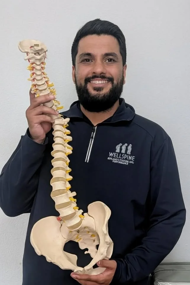 An asian man smiling holding a spine and pelvis model