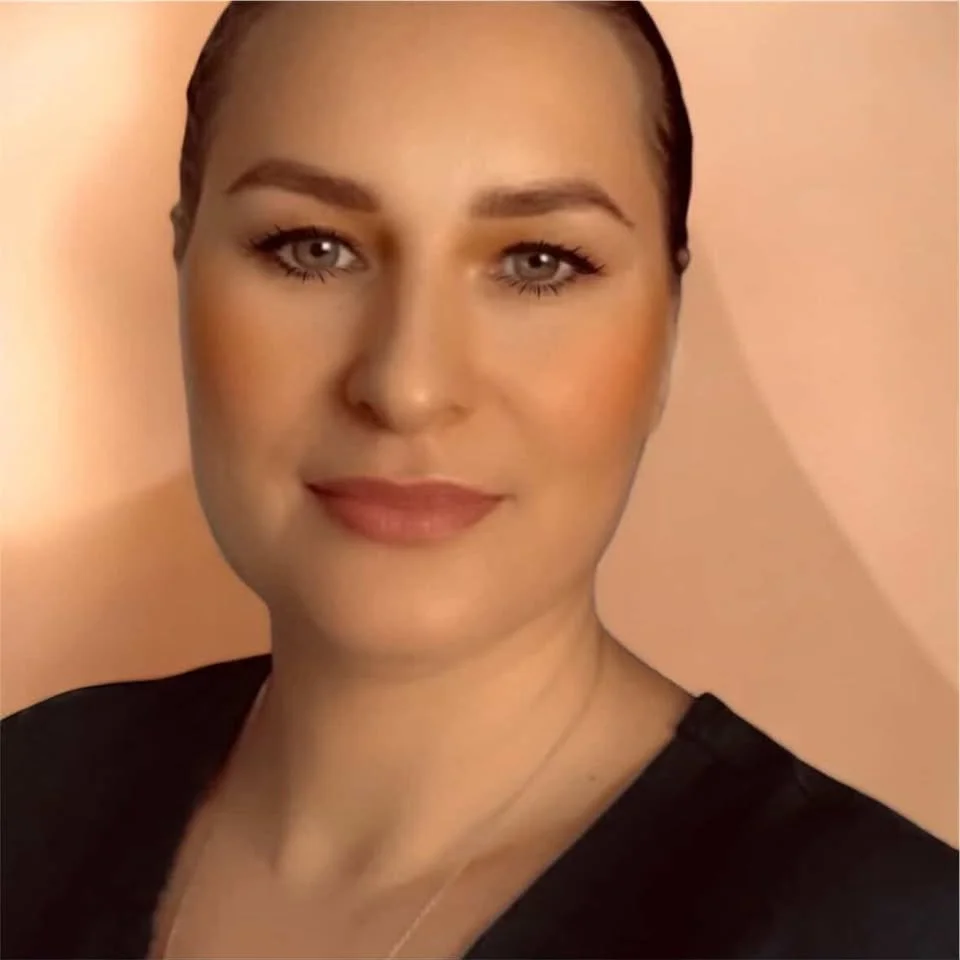 White lady with hair pulled back into a bun, smiling in front of a peach wall
