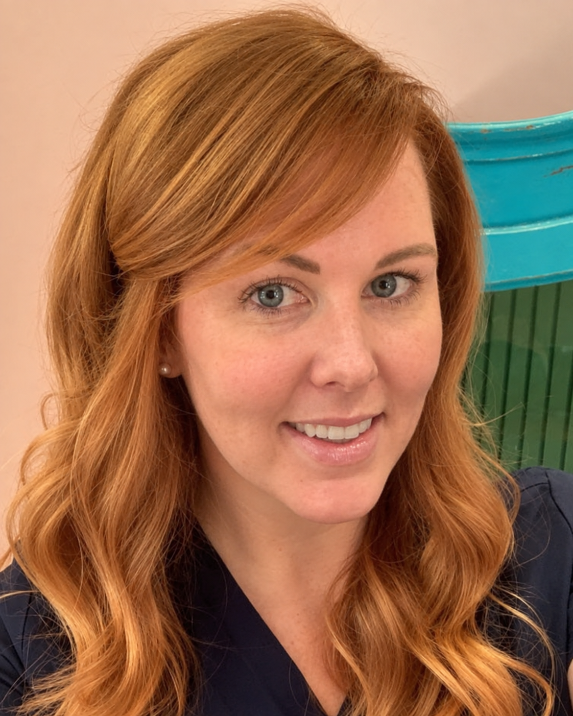 Red headed long curly haired young lady smiling at the camera in dark blue scrubs
