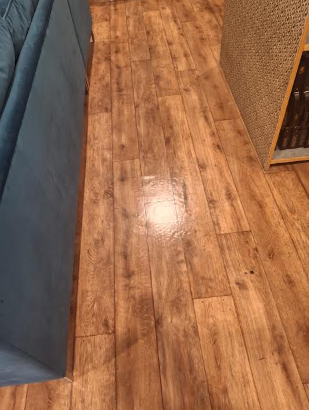 Wooden floor with a section of a blue couch on the left and a wooden cabinet or bookshelf on the right.