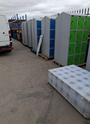 Row of public lockers in various colors, along with a mattress and a white van parked nearby.