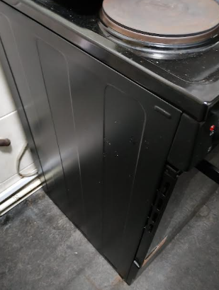 Black metal stove or oven with a round cooking surface on top, positioned in a kitchen against the wall.