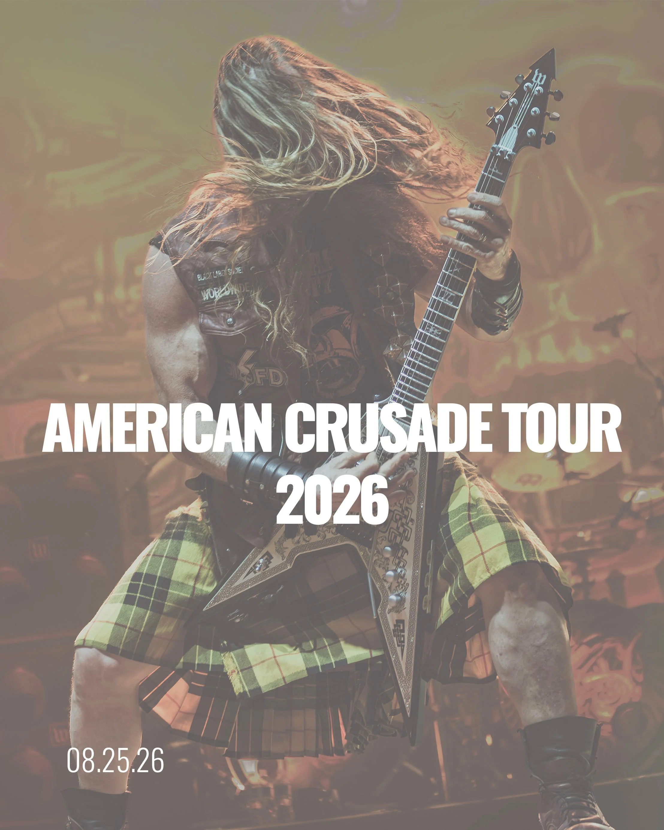A guitarist with long, blonde hair playing on stage during the American Crusade Tour in 2026. The musician is wearing a plaid kilt, a leather vest, and black boots, with a tattooed arm visible. The background features flames with orange and yellow hues, and there is a band logo or artwork on the vest.