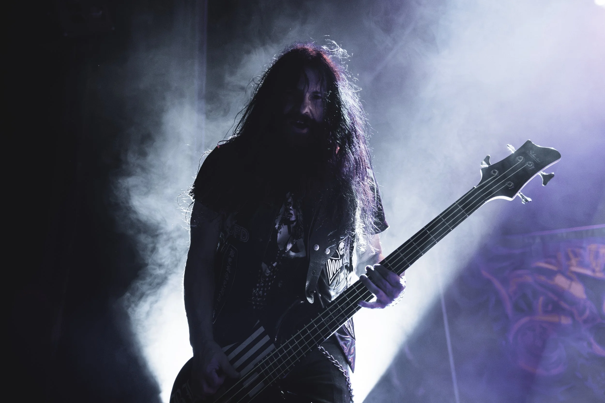 A long-haired male guitarist performing on stage with dramatic lighting and fog, playing an electric guitar.