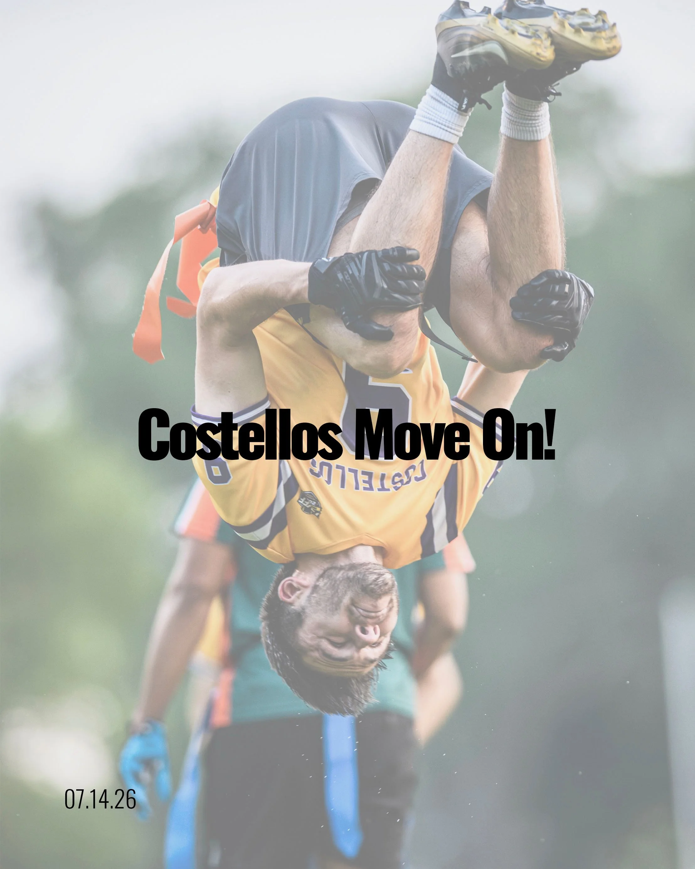 A young man in a sports uniform performs a handstand or gymnastic move outdoors on a grass field while holding a blue pole, with his face turned downward and his arms supporting his body, against a blurred background of cloudy sky and trees.
