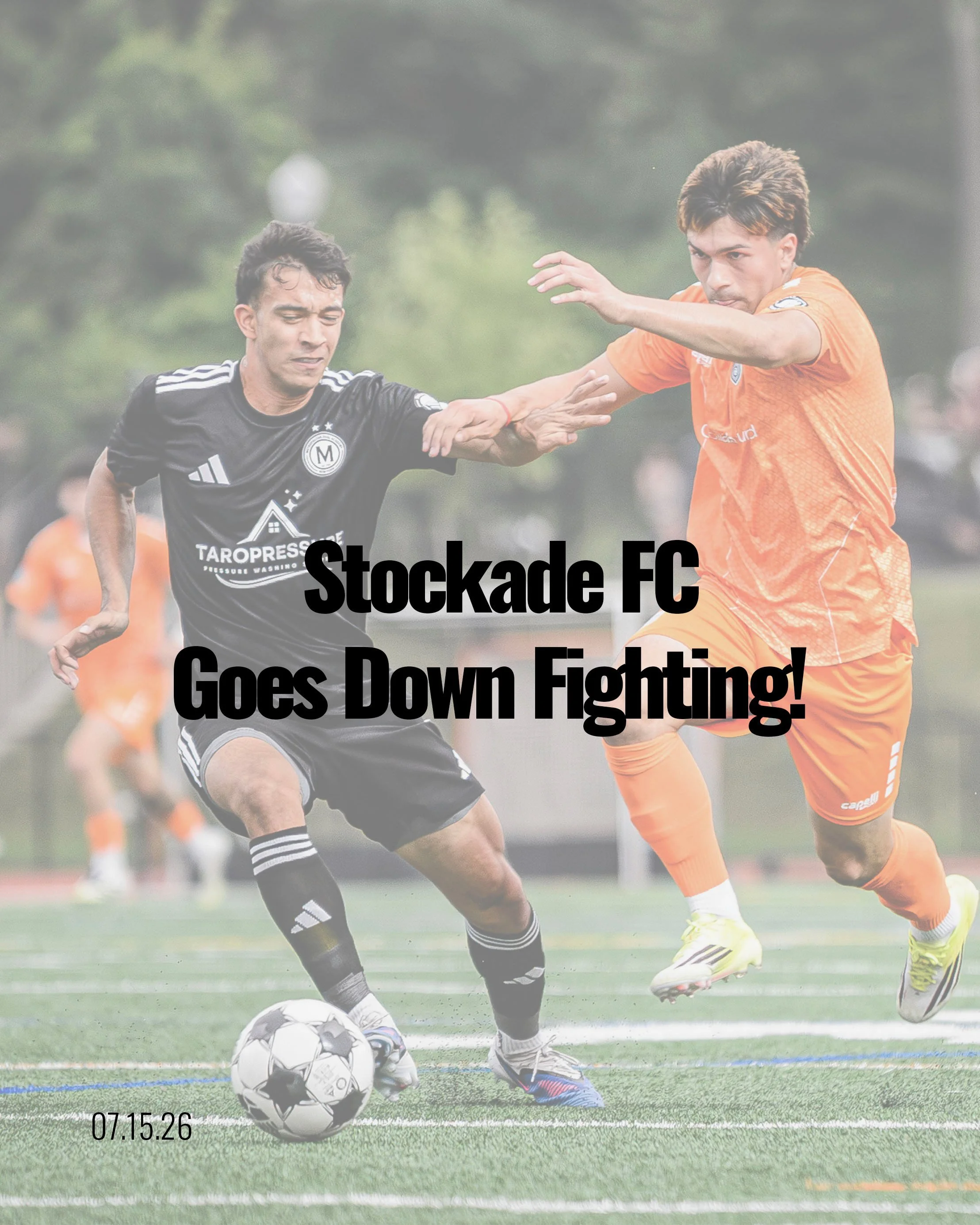 Two soccer players, one in black and the other in orange, competing for control of a soccer ball on a green field with trees in the background. The player in black is trying to kick the ball while the player in orange is making a move to block or challenge him.