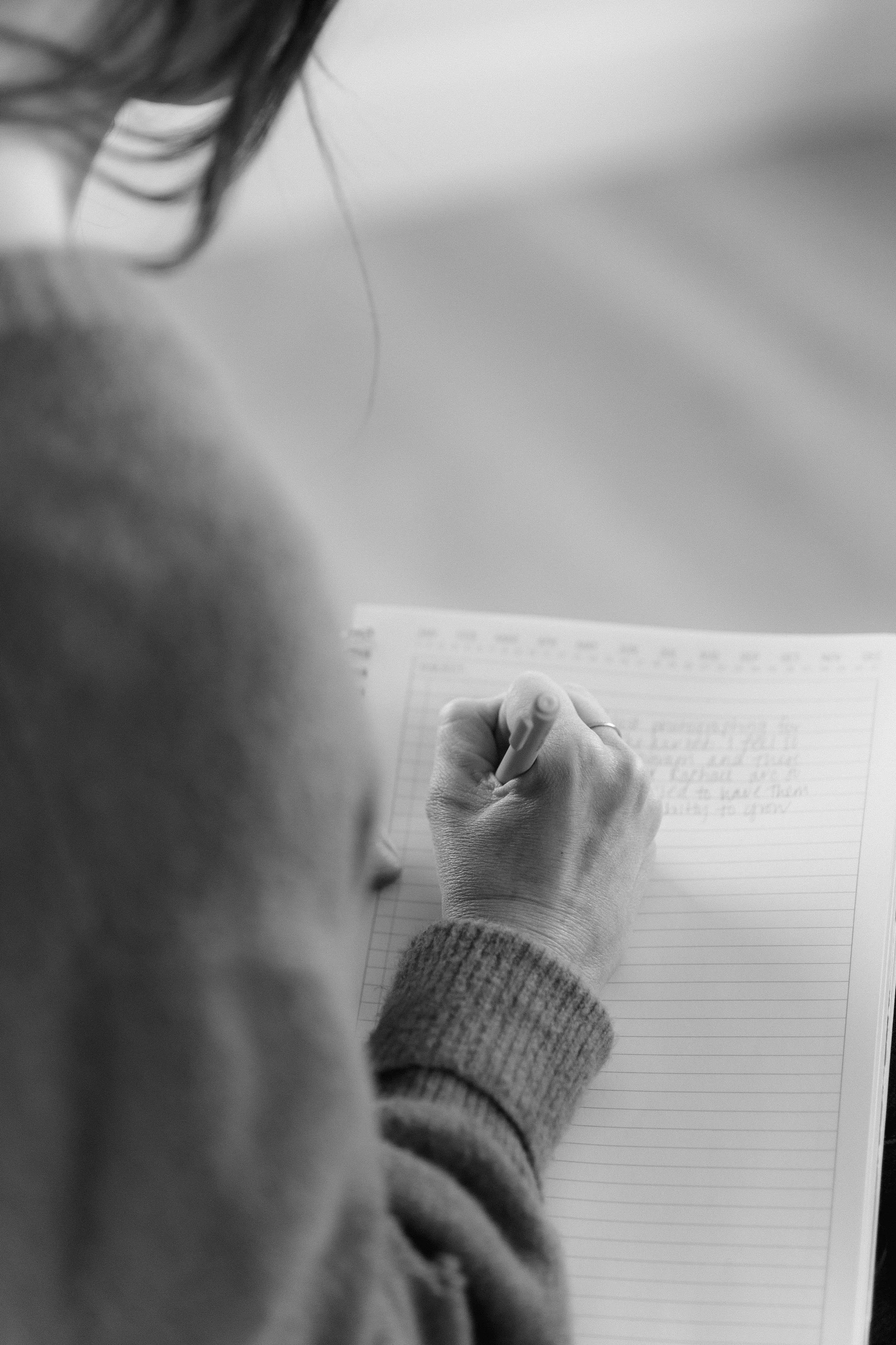 A person writing in a notebook with a pen, seen from above in black and white.
