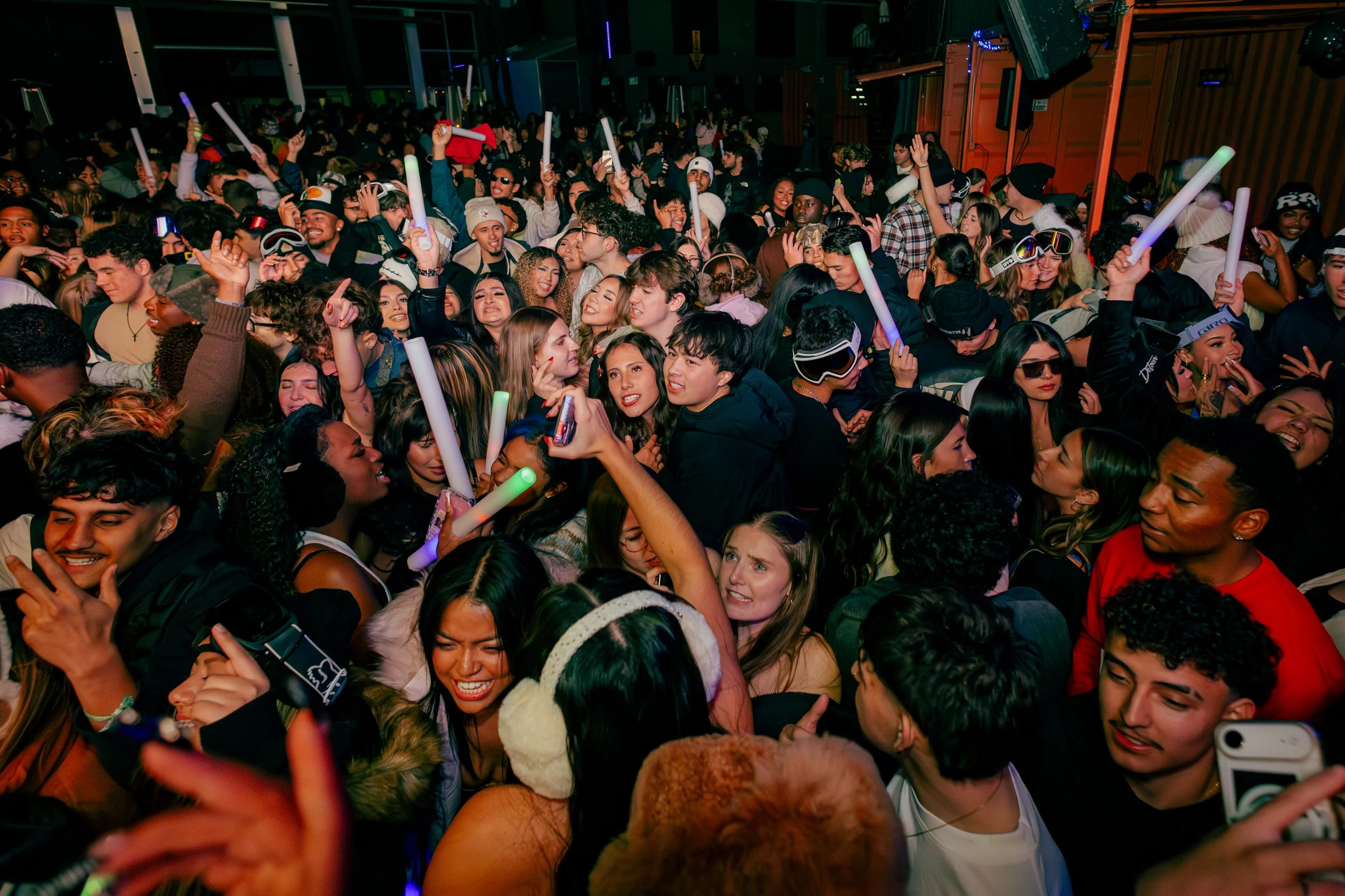 Crowded dance floor with young people dancing and holding glow sticks at a lively party or concert.