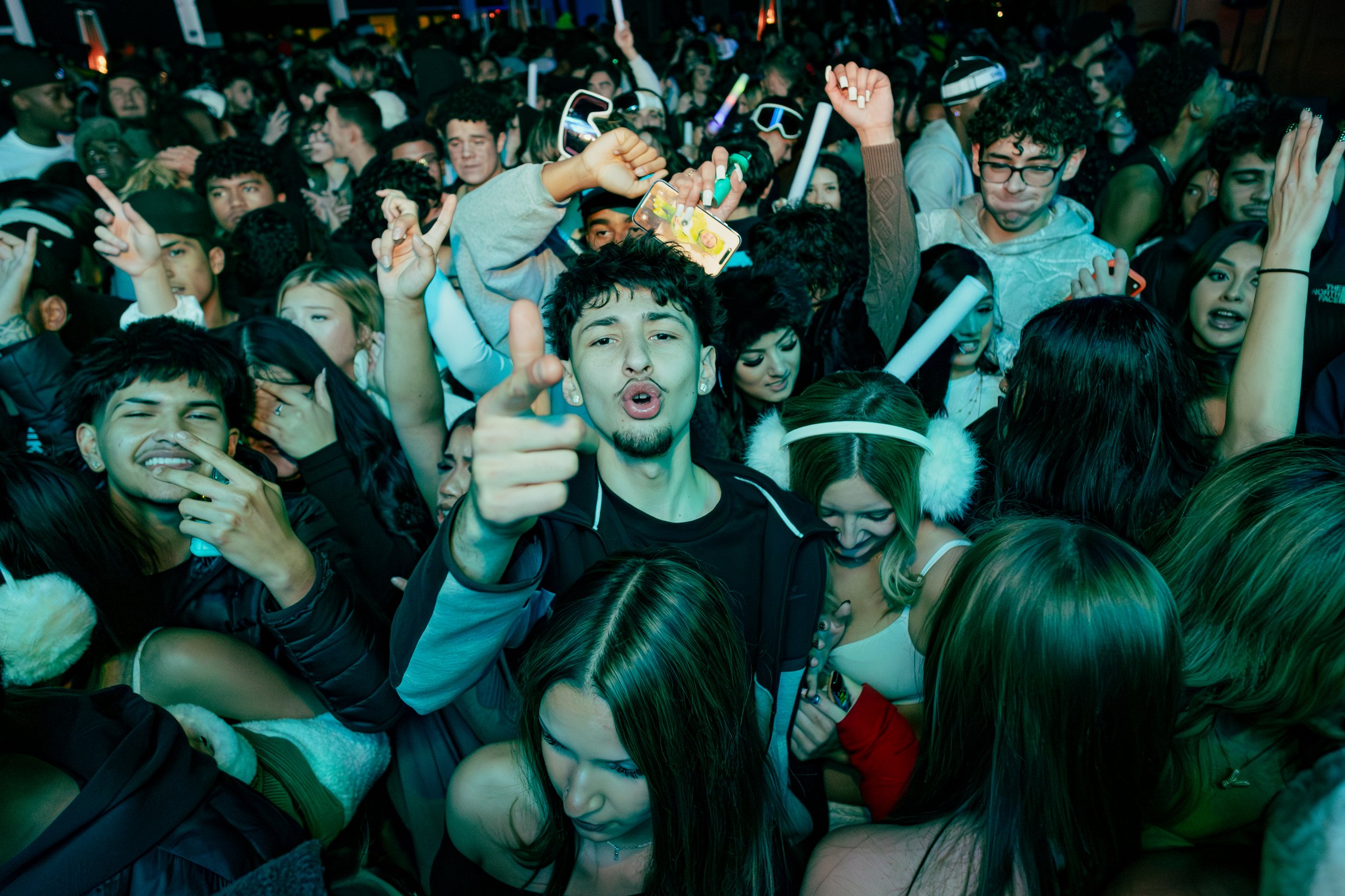 Crowd of young people at a concert or festival, with some singing, dancing, and taking photos, creating a lively and energetic atmosphere.
