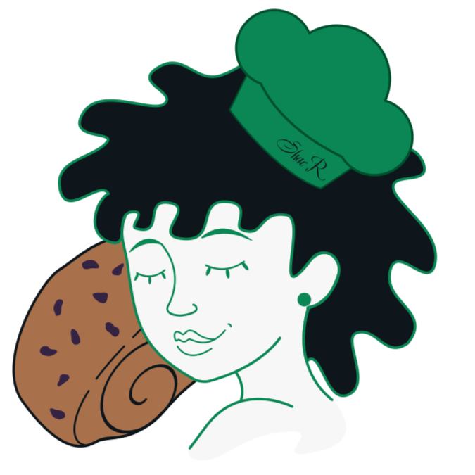 A woman with short curly black hair wearing a chef's hat that says "Blue R", holding a large chocolate chip cookie near her face, with her eyes closed and smiling.
