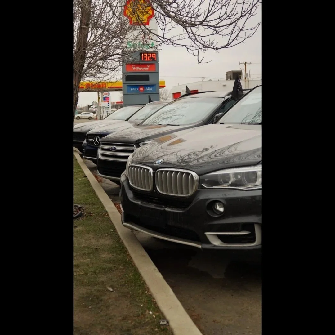 A row of parked cars, including a BMW and a Mercedes-Benz, at a dealership